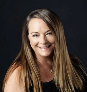 Woman with long brown hair smiles at the camera against a dark background.