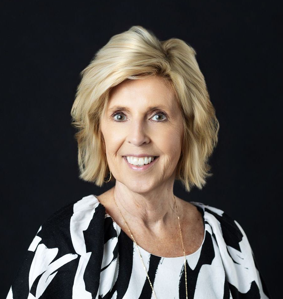 Blonde woman with a warm smile in a black and white patterned top against a black background.