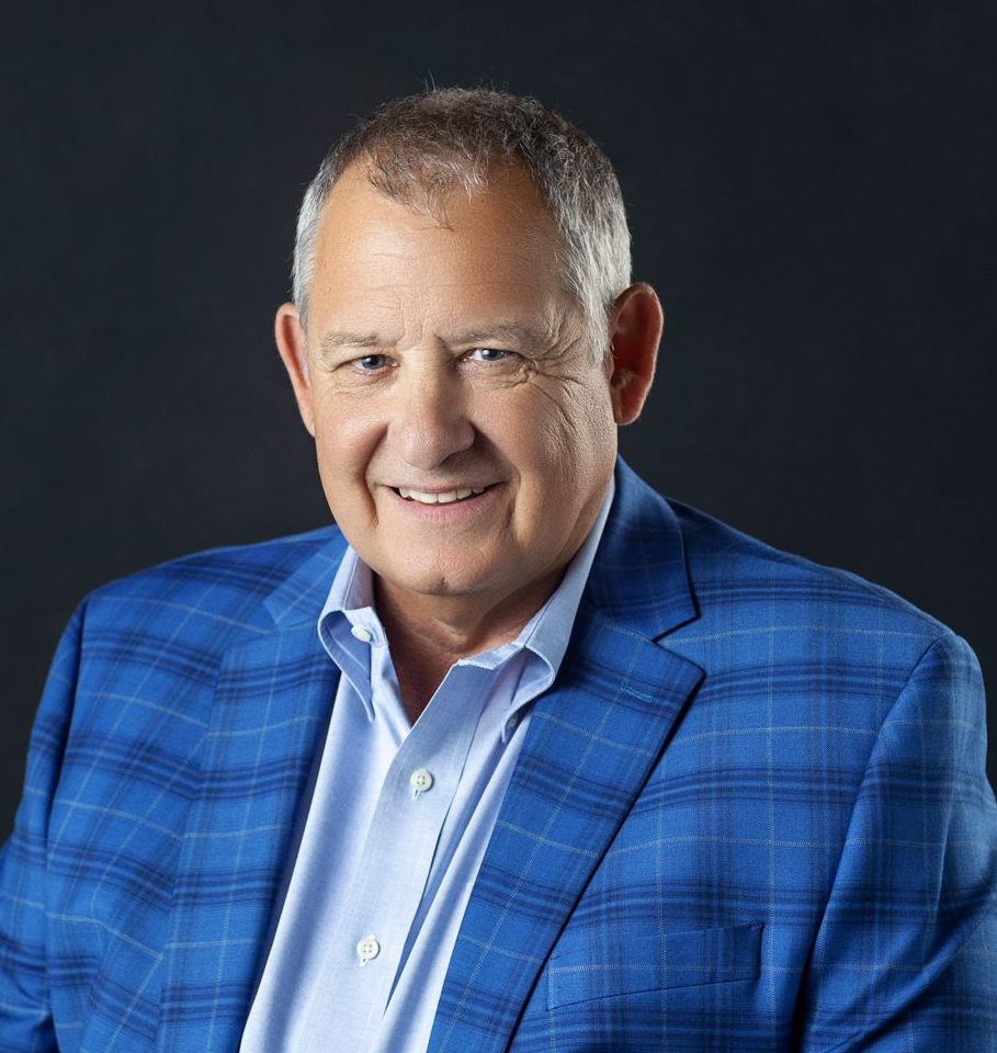 Smiling man in a blue plaid blazer and light blue shirt against a dark background.