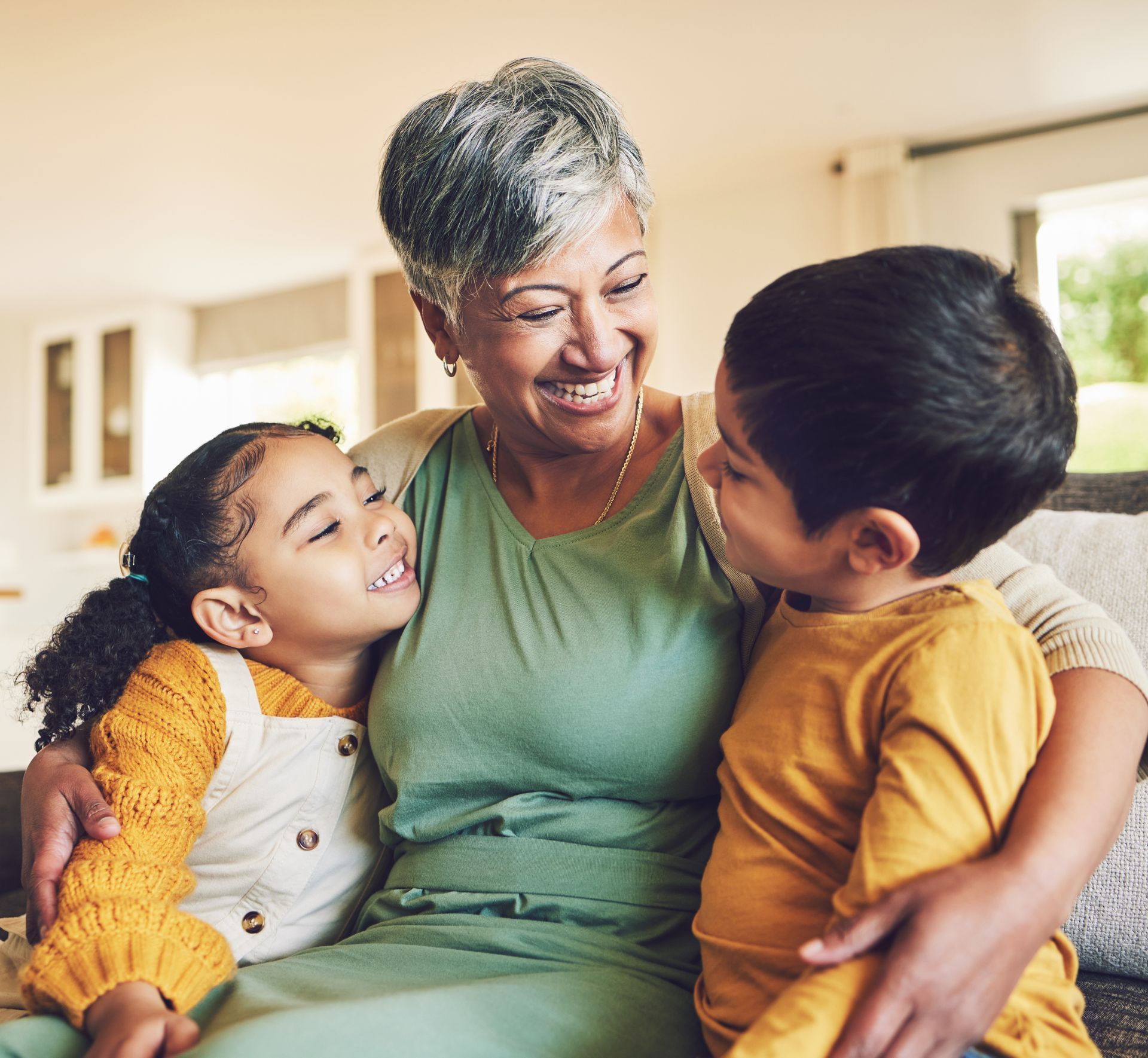 Grandmother smiles, embraces two children on a couch.
