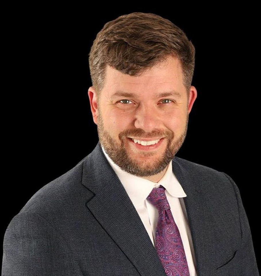 Smiling man in a suit and purple tie on a black background.