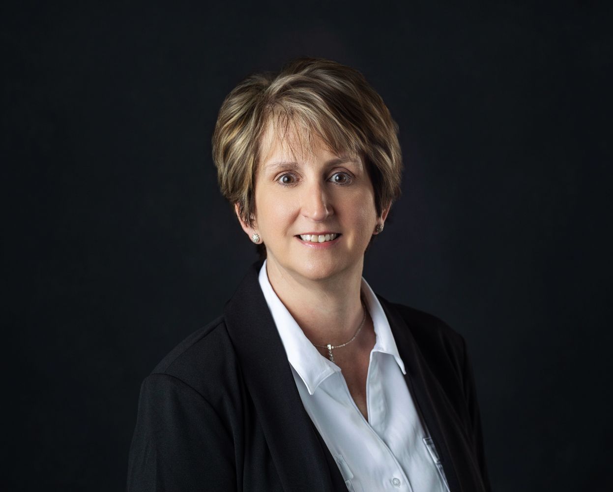 Woman in blazer and white shirt smiles against a dark background.