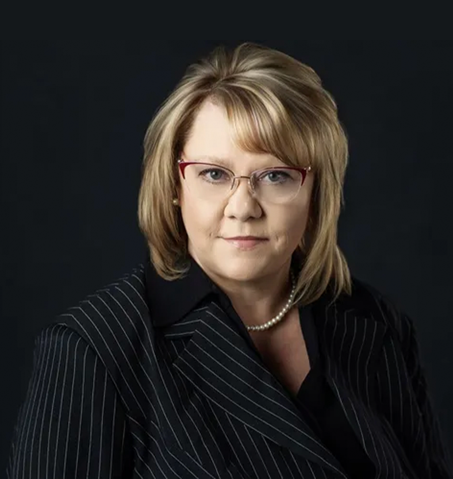 Woman in suit, red glasses, looking at the viewer, studio shot with dark background.