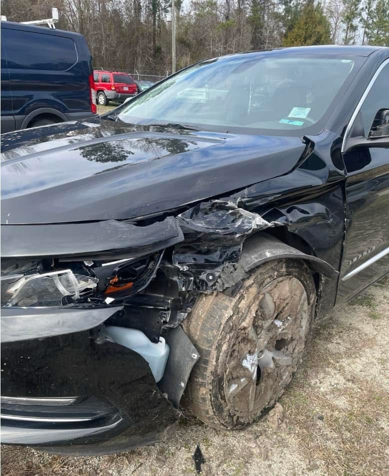 Damaged black car with front-end collision damage to the left side, including the tire and fender.