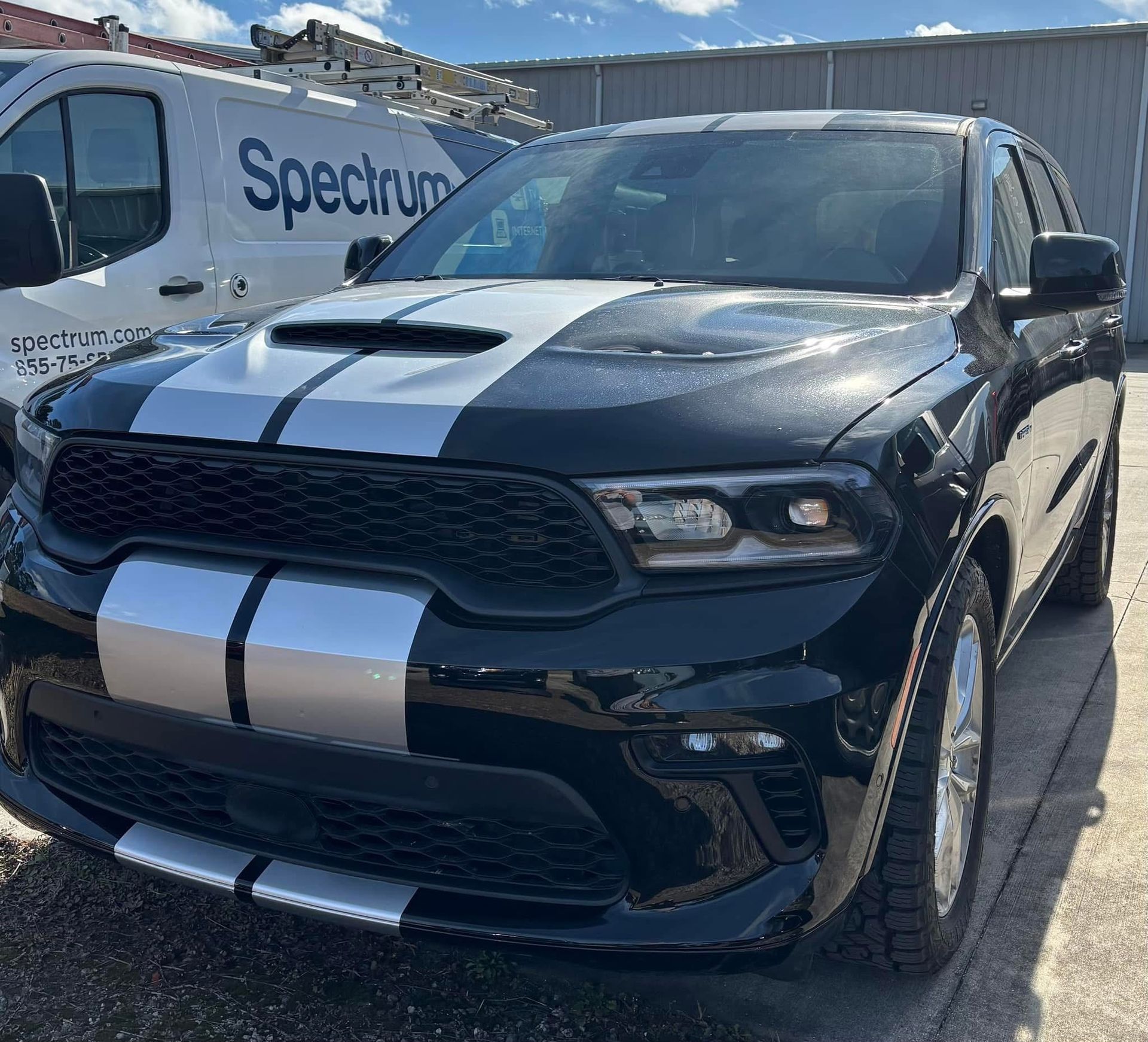Black Dodge Durango SUV with silver racing stripes parked next to a Spectrum van.