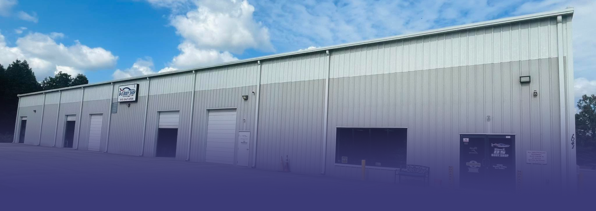 A long, metal industrial building with a blue sky and white clouds.