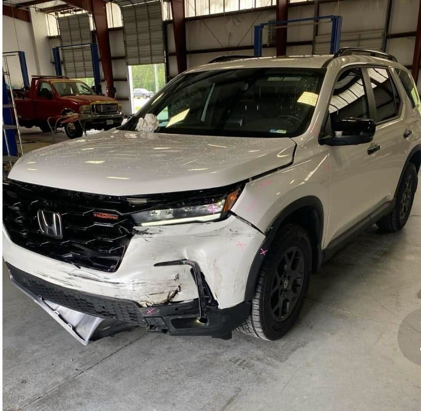 White Honda SUV with front-end damage in an auto repair shop.