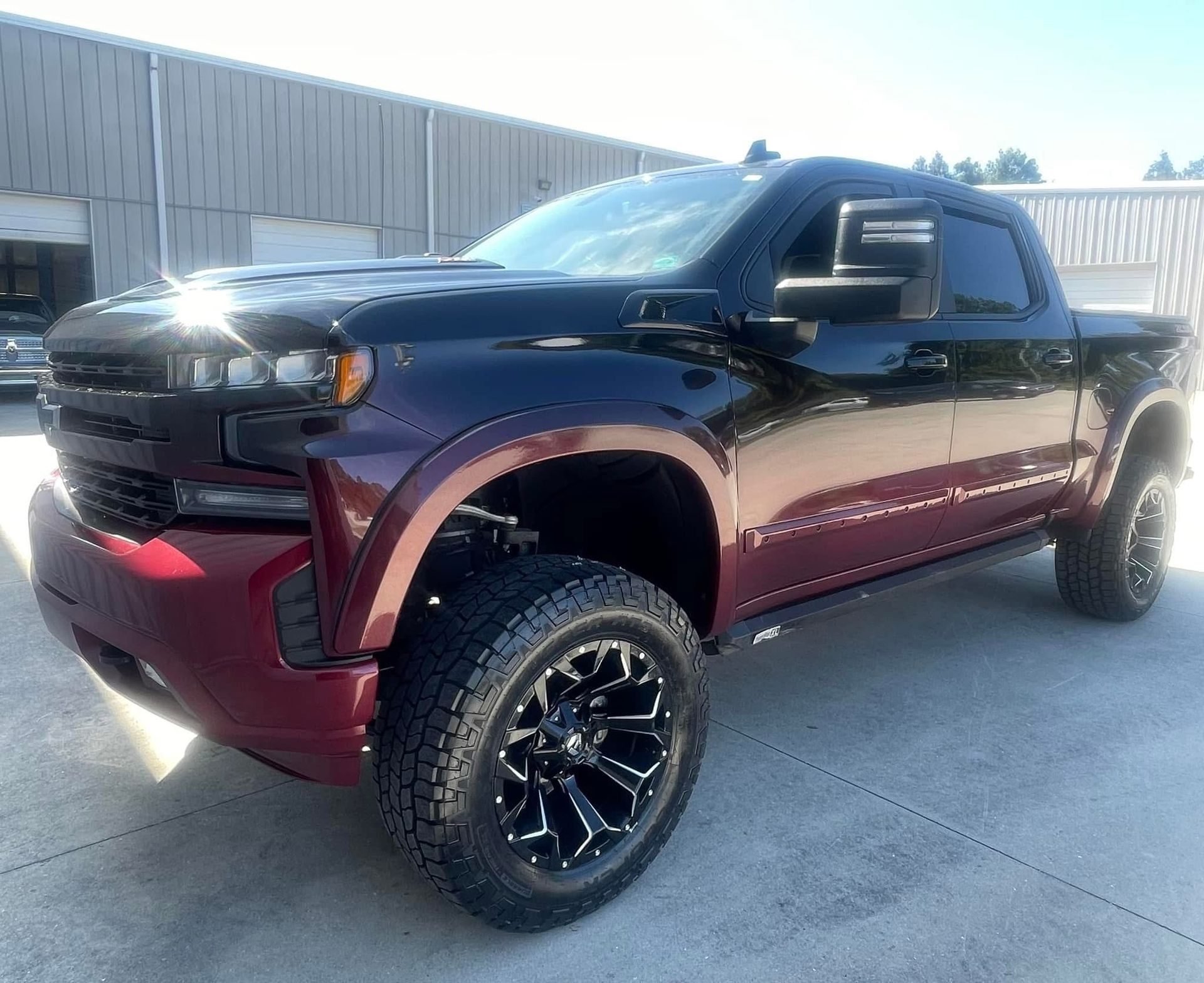 Black and maroon Chevrolet Silverado pickup truck, lifted with large tires, parked in front of a building.