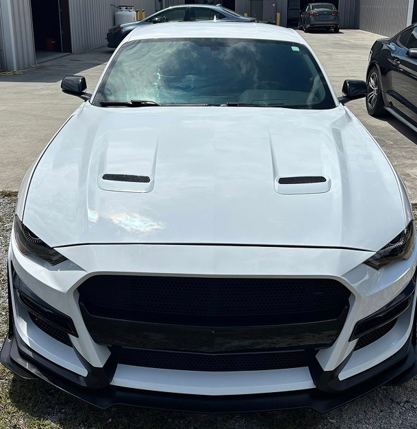 White Ford Mustang with black grille and hood vents, parked outside.