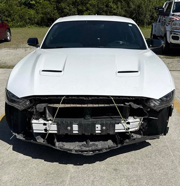 White Mustang car with front bumper damage, parked outdoors.