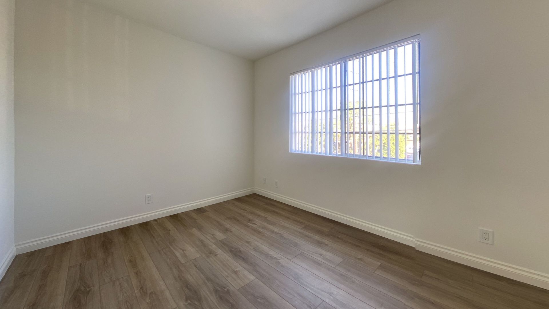 Empty room with wood-look flooring, white walls, and a window with bars.