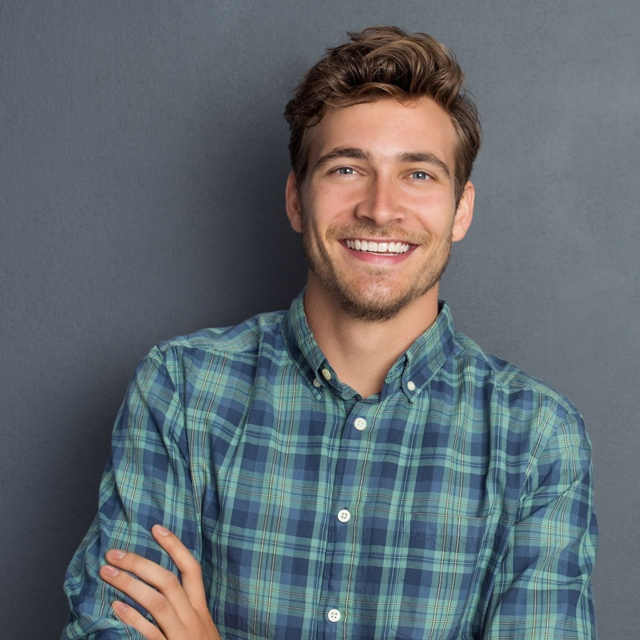 A man in a plaid shirt is smiling with his arms crossed.
