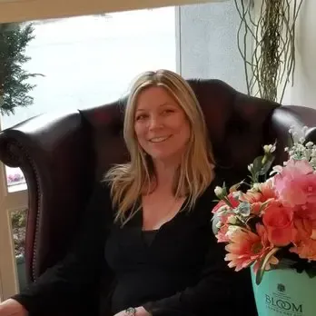 A woman is sitting in a chair next to a vase of flowers.