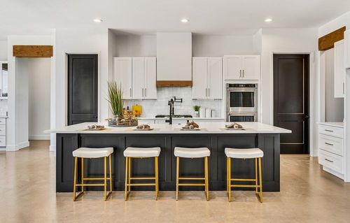 Modern kitchen with white cabinets, black island with gold stools, stainless steel appliances.