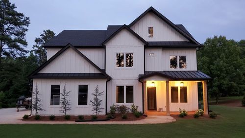 Two-story white house with black trim, entry porch, and black roof. Lit windows and landscaping.