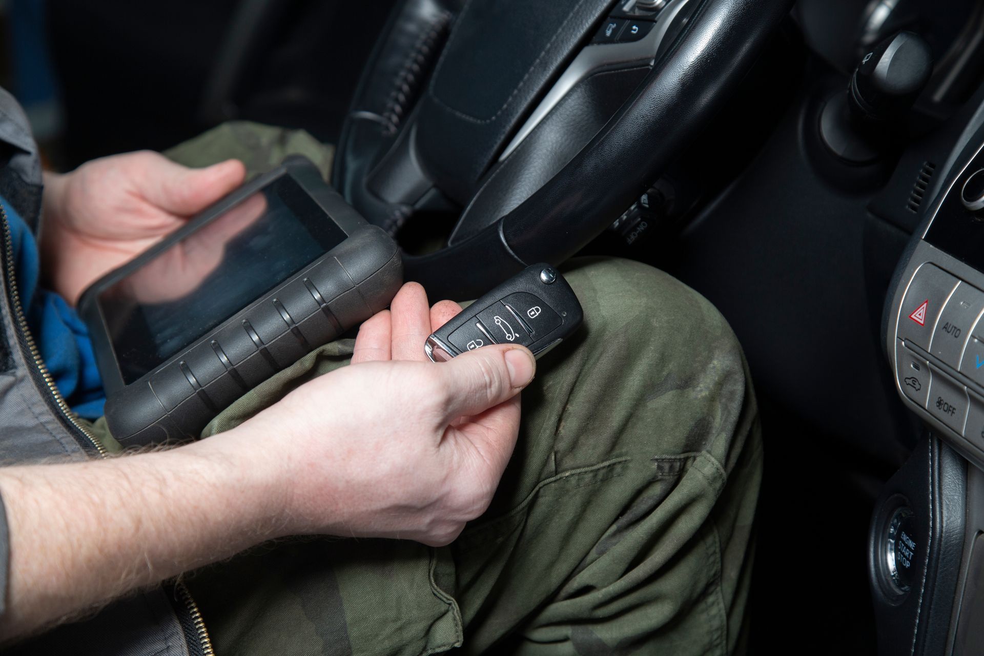 Person holding a handheld device and car key inside a vehicle, with a tablet on their lap