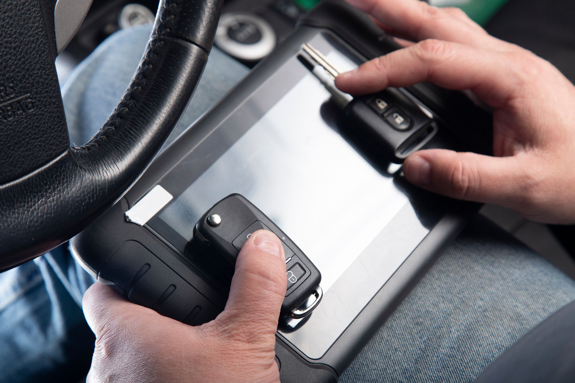 Hands holding a tablet with a stylus in a car, near the steering wheel.