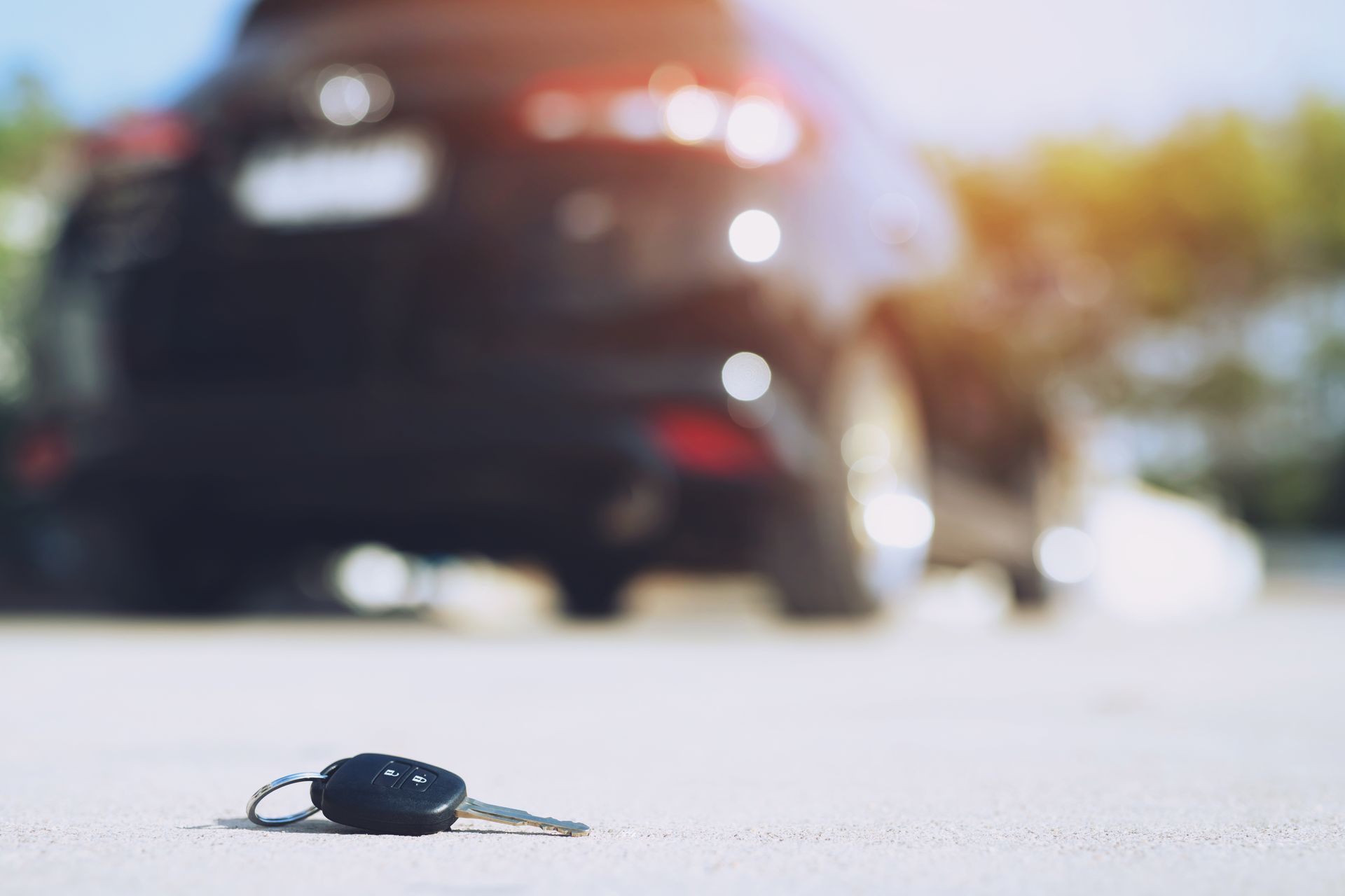 Car key on pavement with blurred car in background, bright sunlight