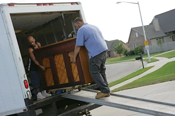 Two people loading a piano into a truck using a ramp.