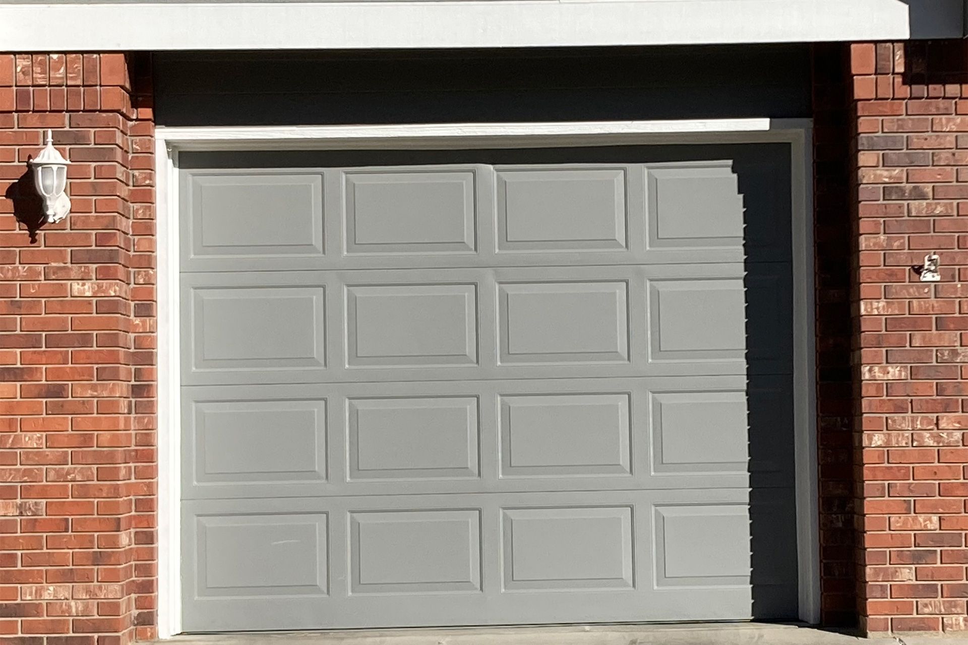 A gray garage door is against a red brick wall