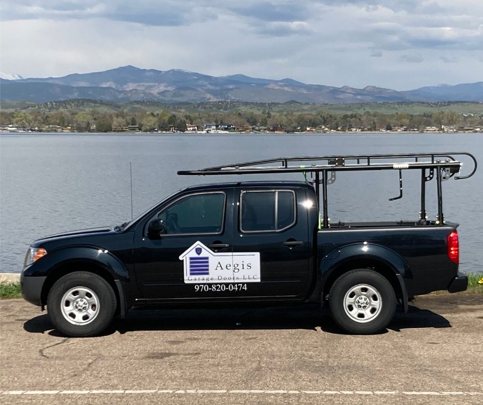 A black truck with a ladder on the back is parked in front of a body of water.