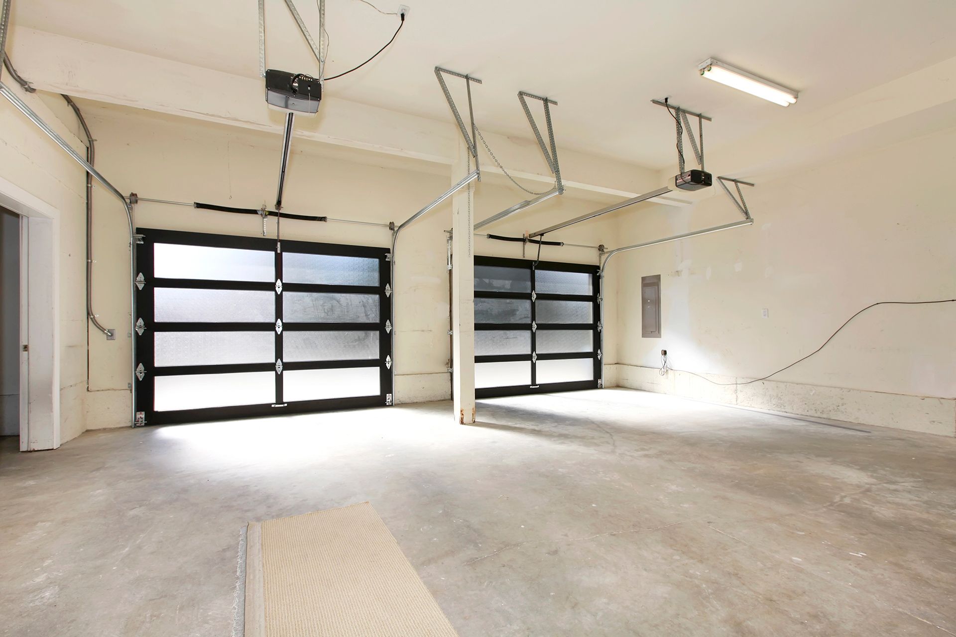 Empty two-car garage with black framed glass doors, concrete floor, white walls.