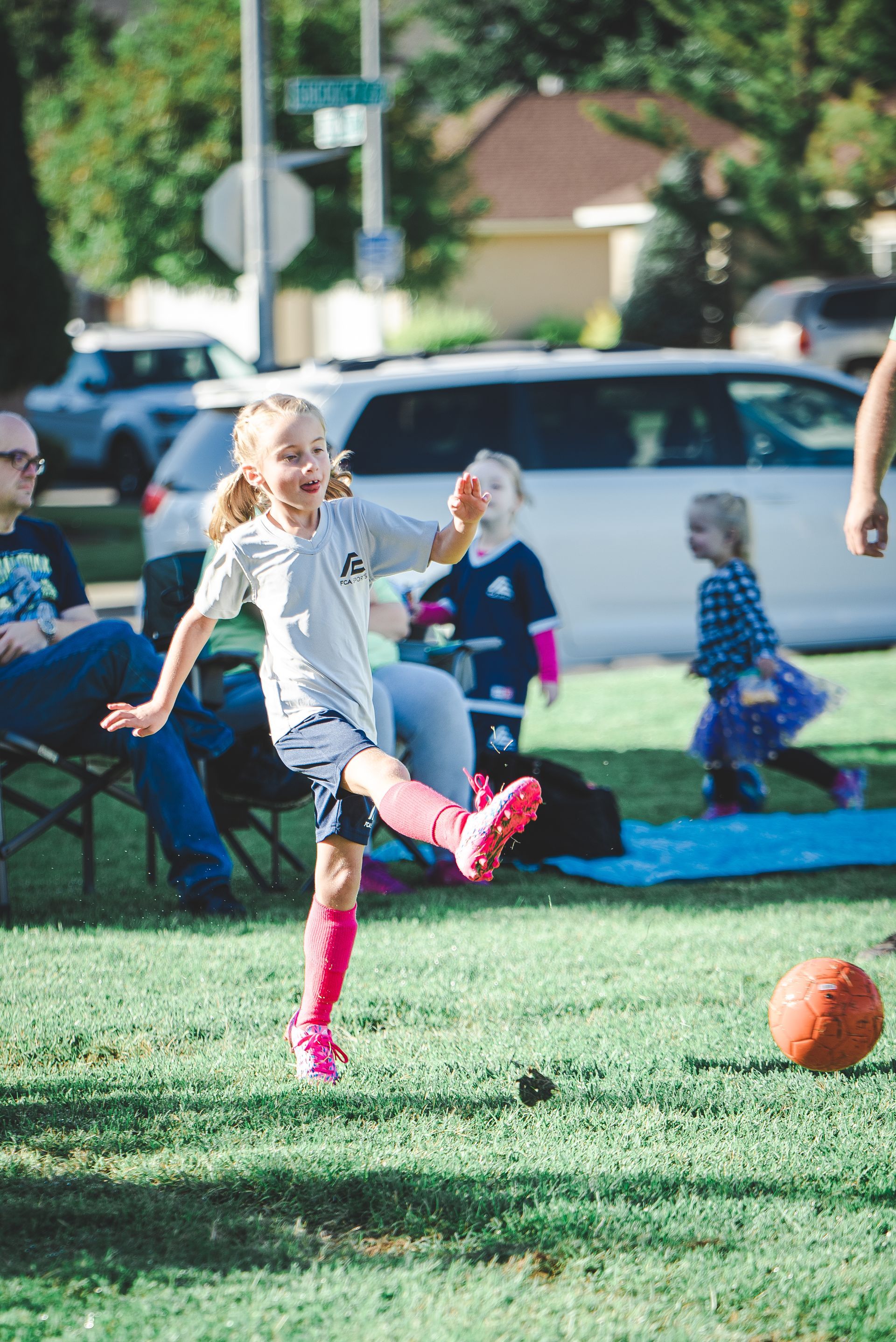 Child kicking an orange ball on a grassy field at an outdoor gathering
