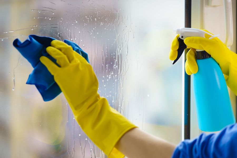 Person in yellow gloves cleaning a window with blue spray and cloth