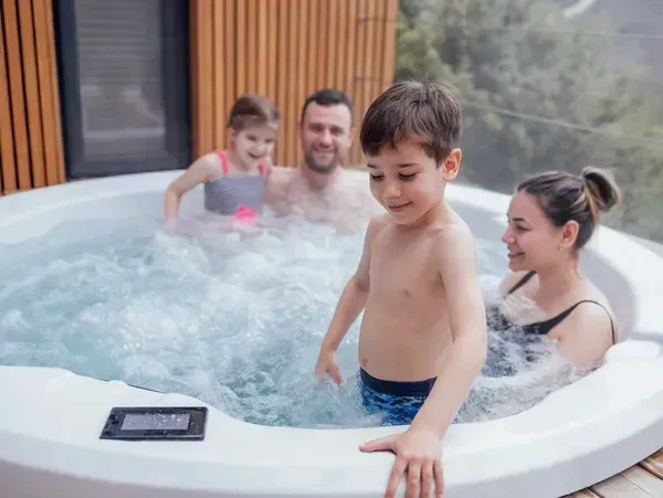 Family relaxing in a bubbling hot tub on a patio, with a child smiling in front