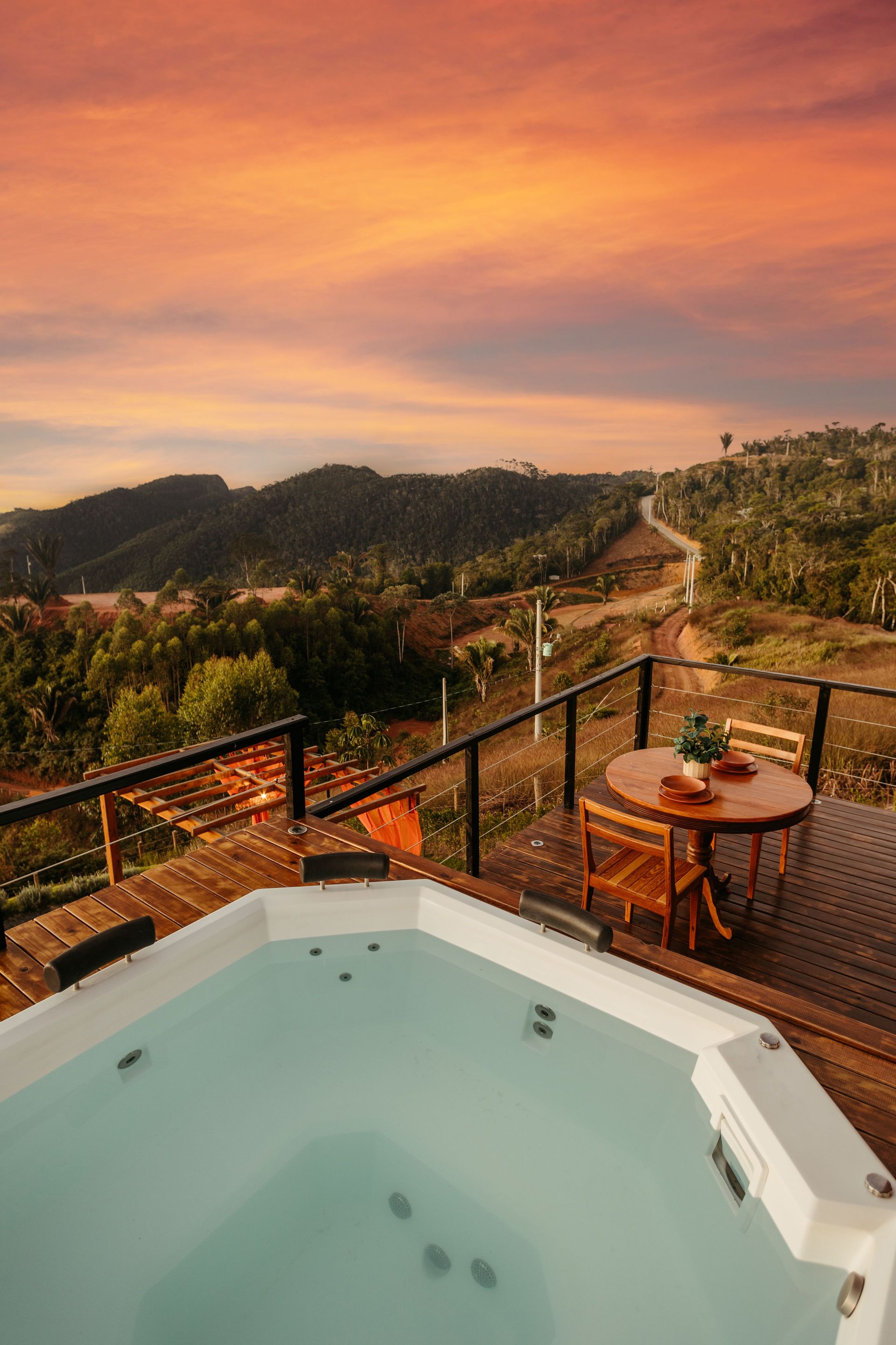 Hot tub on a deck overlooking a sunlit valley at sunset with orange and pink skies