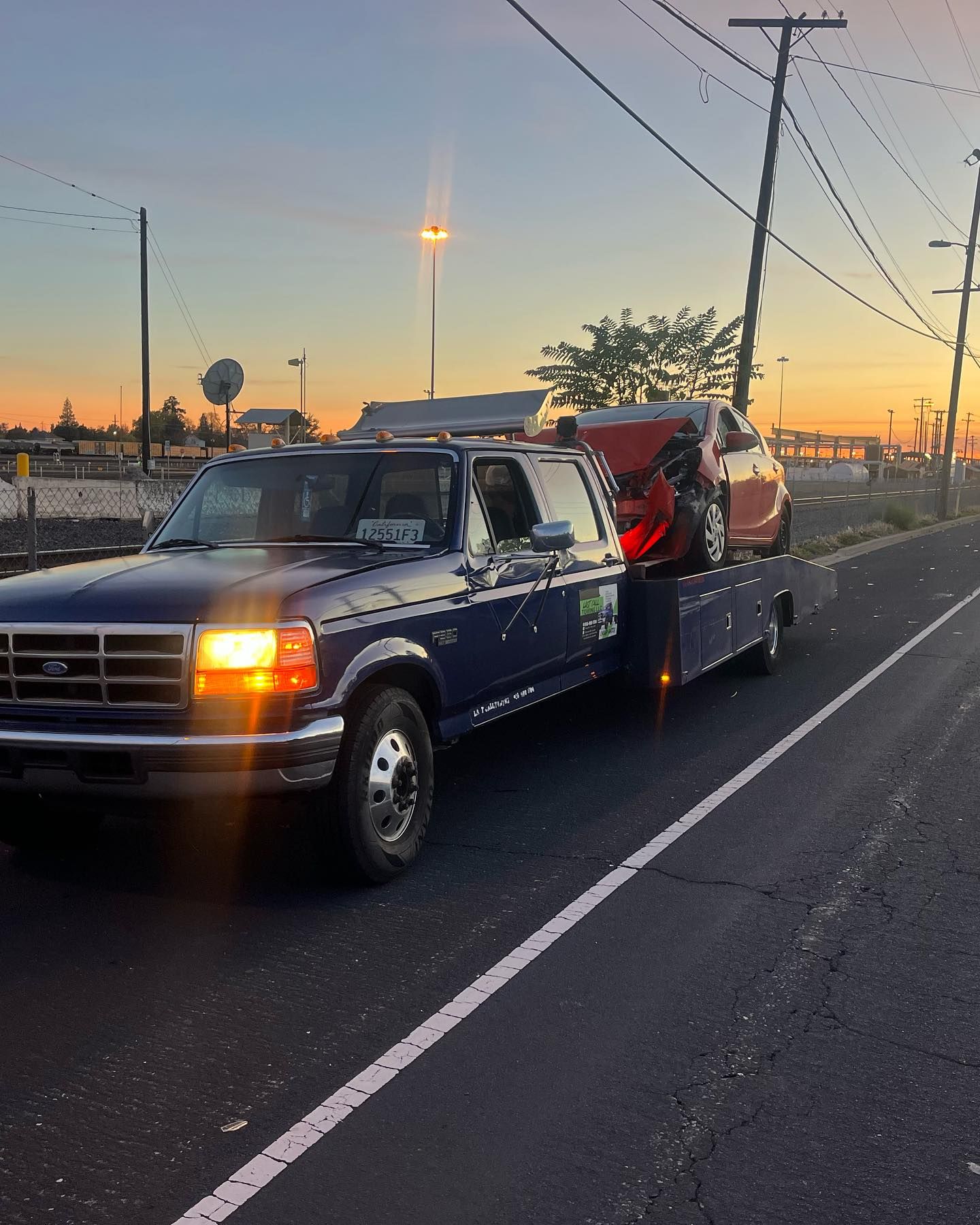 Tow truck hauling a blue sedan at sunset on a roadside
