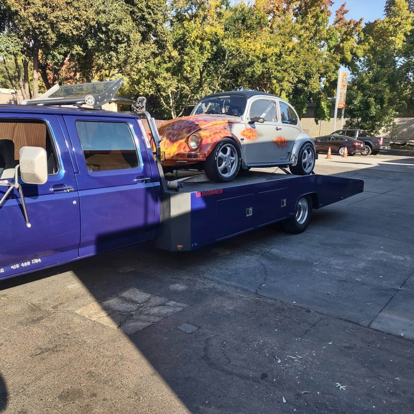 Purple tow truck carrying an orange-and-white Volkswagen Beetle on its flatbed outdoors