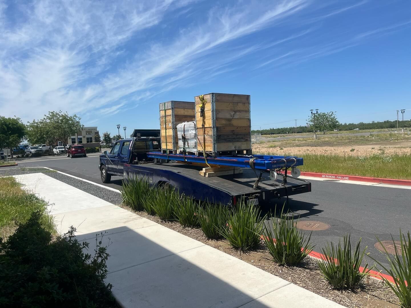 Flatbed truck carrying stacked crates on a sunny roadside with blue sky and dry grass