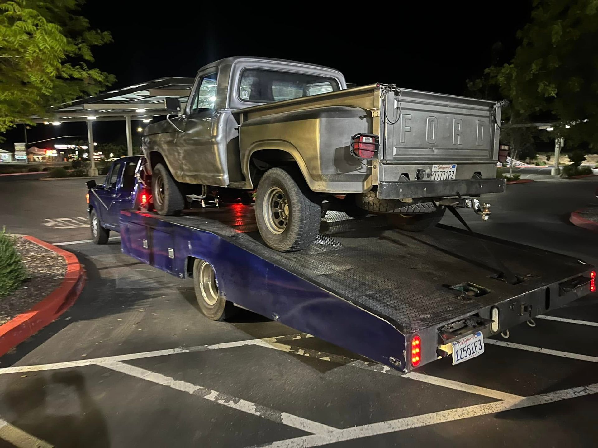 Silver pickup truck on a blue flatbed tow trailer at night in a parking lot