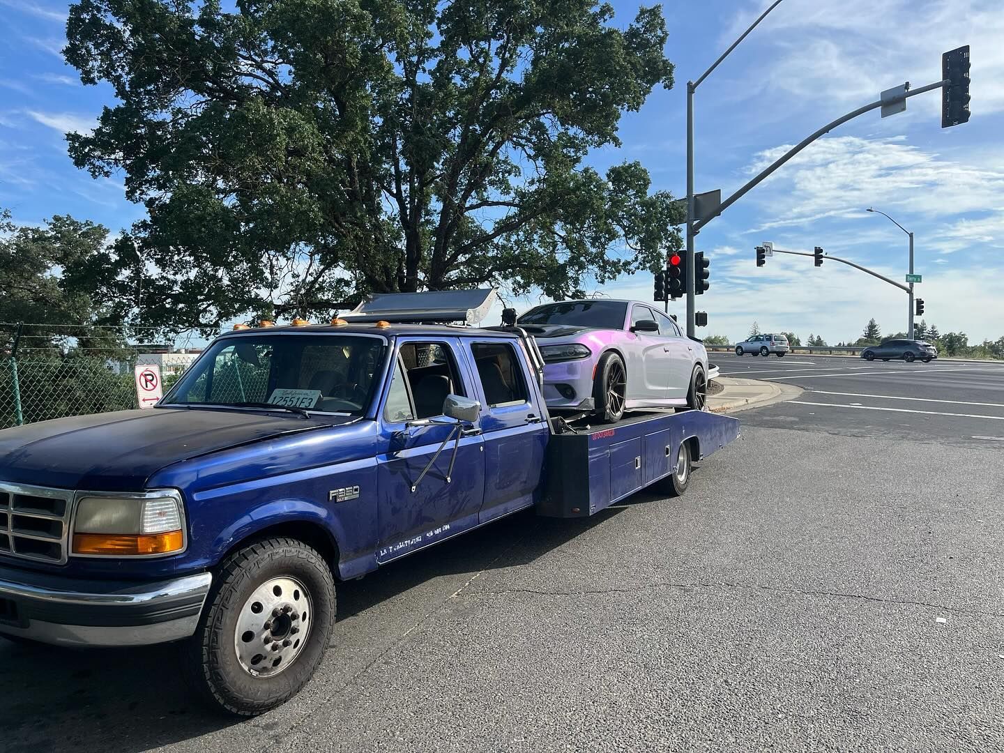 Blue tow truck hauling a pink car at a traffic light on a city street