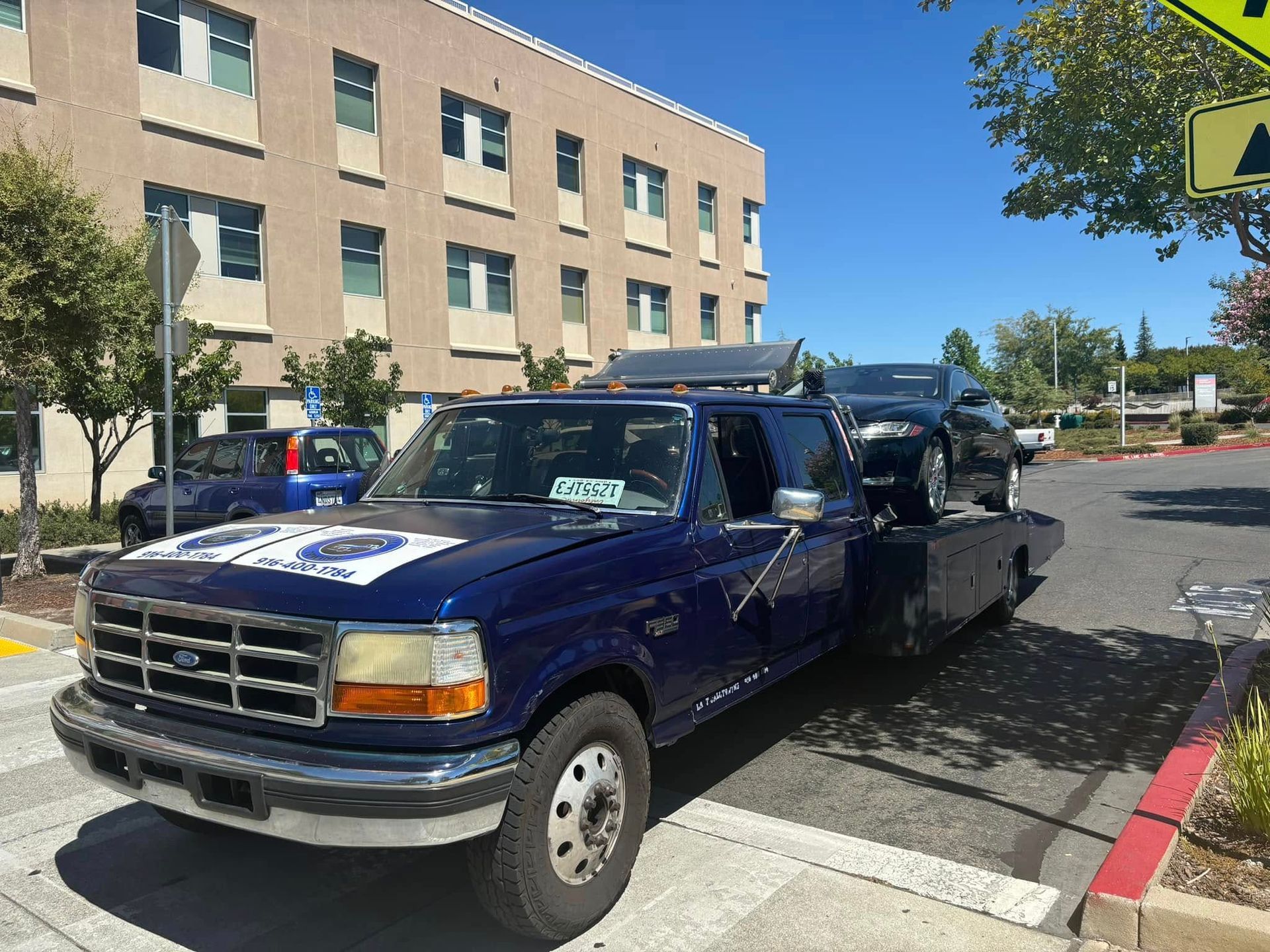 Blue pickup truck parked in a lot beside a tan office building on a sunny day