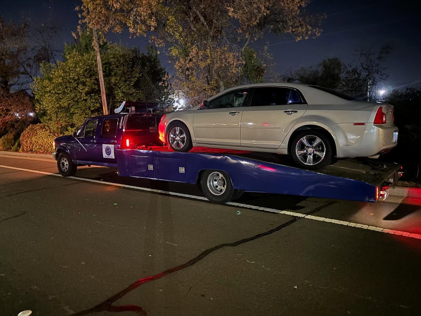 White sedan on a purple tow truck at night on a city street