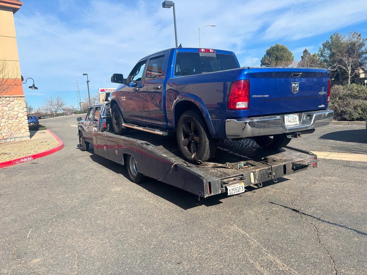 Blue pickup truck on a tilted flatbed tow trailer in a parking lot under a clear sky