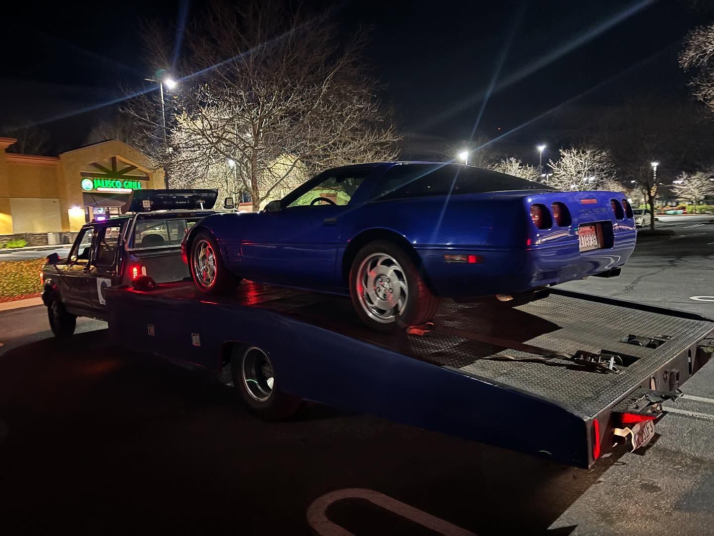 Blue sports car on a tow truck at night in a parking lot