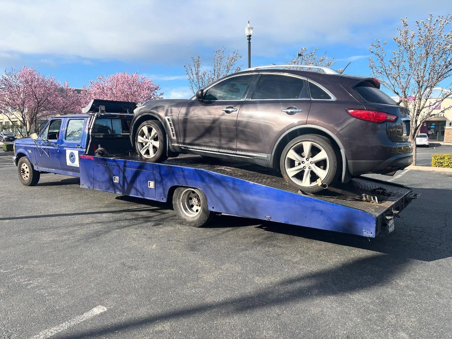 Black SUV loaded on a blue flatbed tow truck in a parking lot