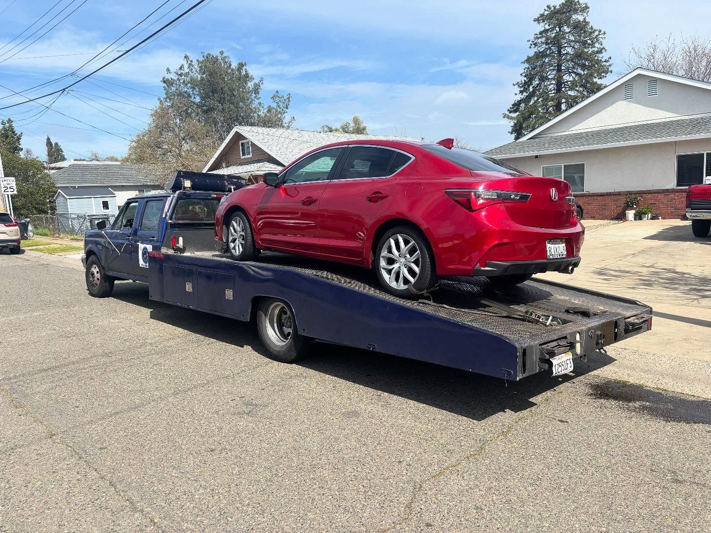 Red sedan strapped on a flatbed tow truck in a residential neighborhood.
