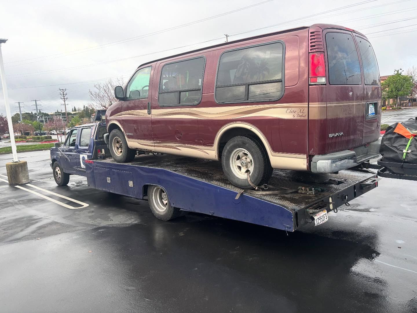 Maroon van being loaded onto a blue flatbed tow truck on a wet road