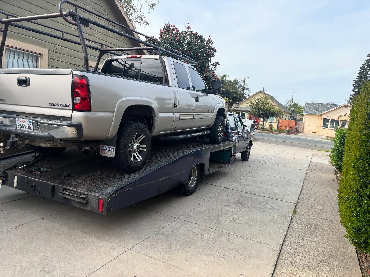 Silver pickup truck loaded on a black car hauler trailer in a driveway near houses