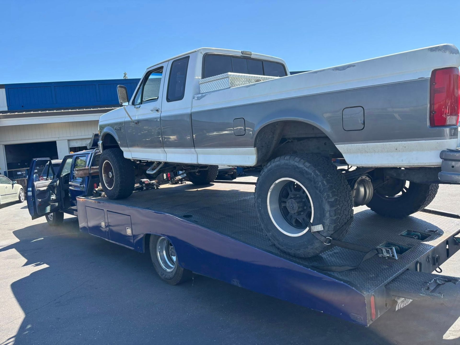 Silver pickup truck on a flatbed tow trailer, parked outdoors under a blue sky.
