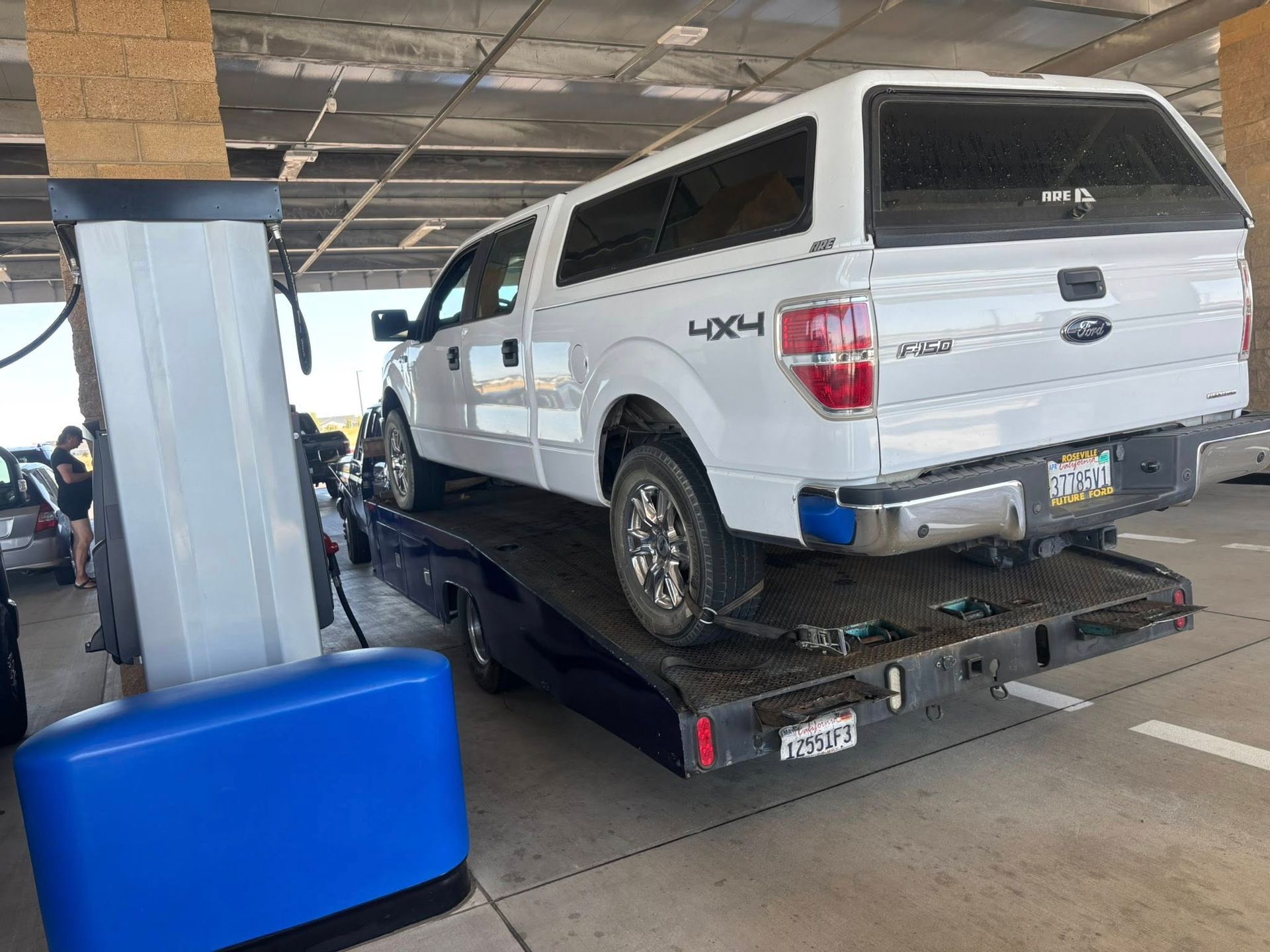 White pickup truck on a flatbed tow truck in a parking garage, with a blue barrier in the foreground