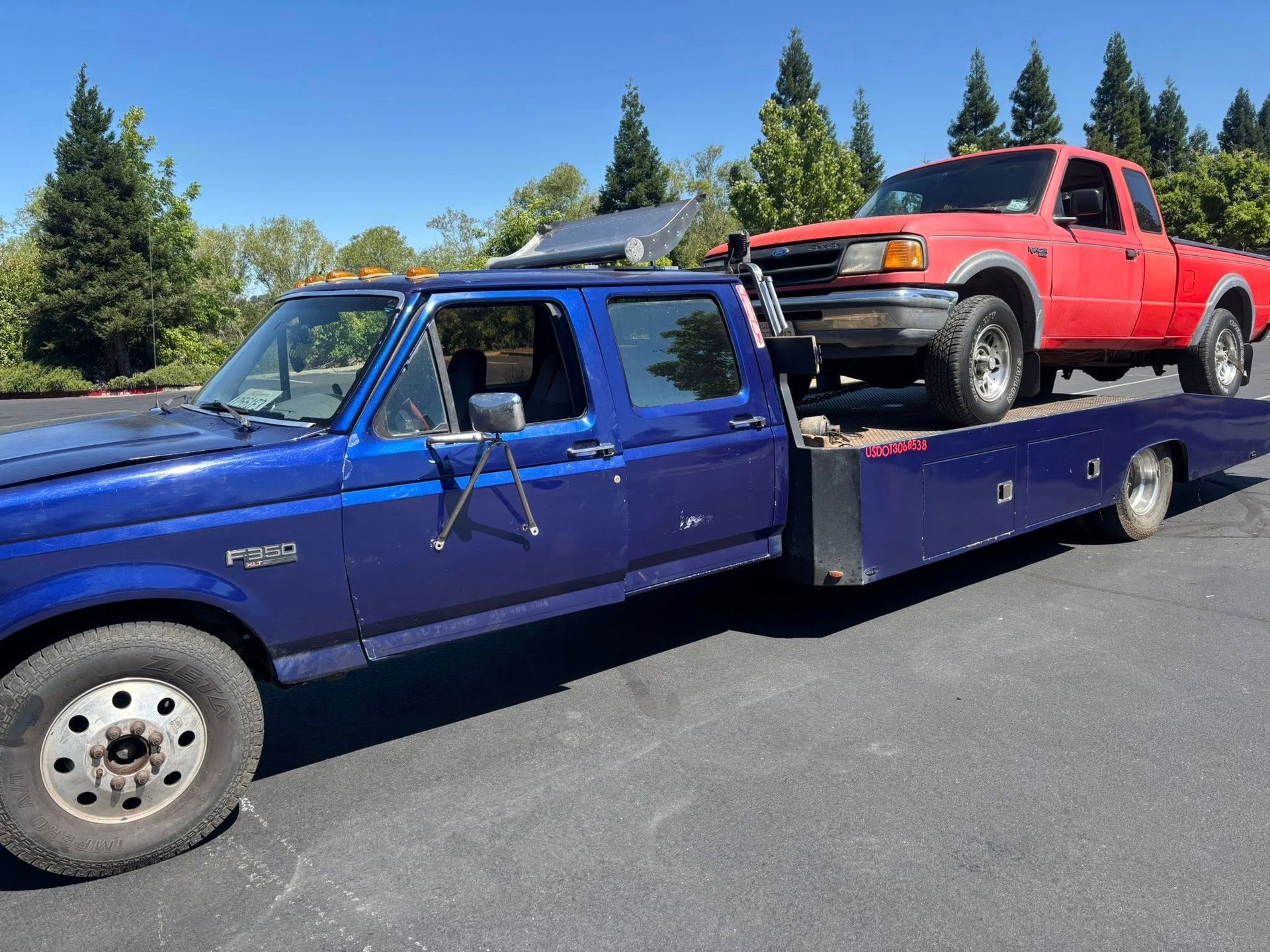 Blue tow truck hauling a red pickup on a flatbed trailer under a clear sky