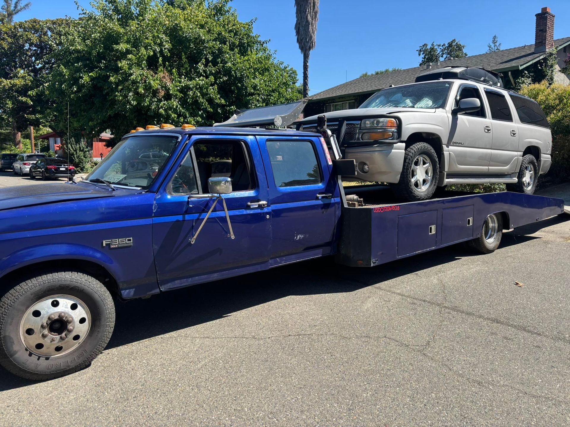 Blue tow truck hauling a beige SUV on a flatbed trailer on a sunny street