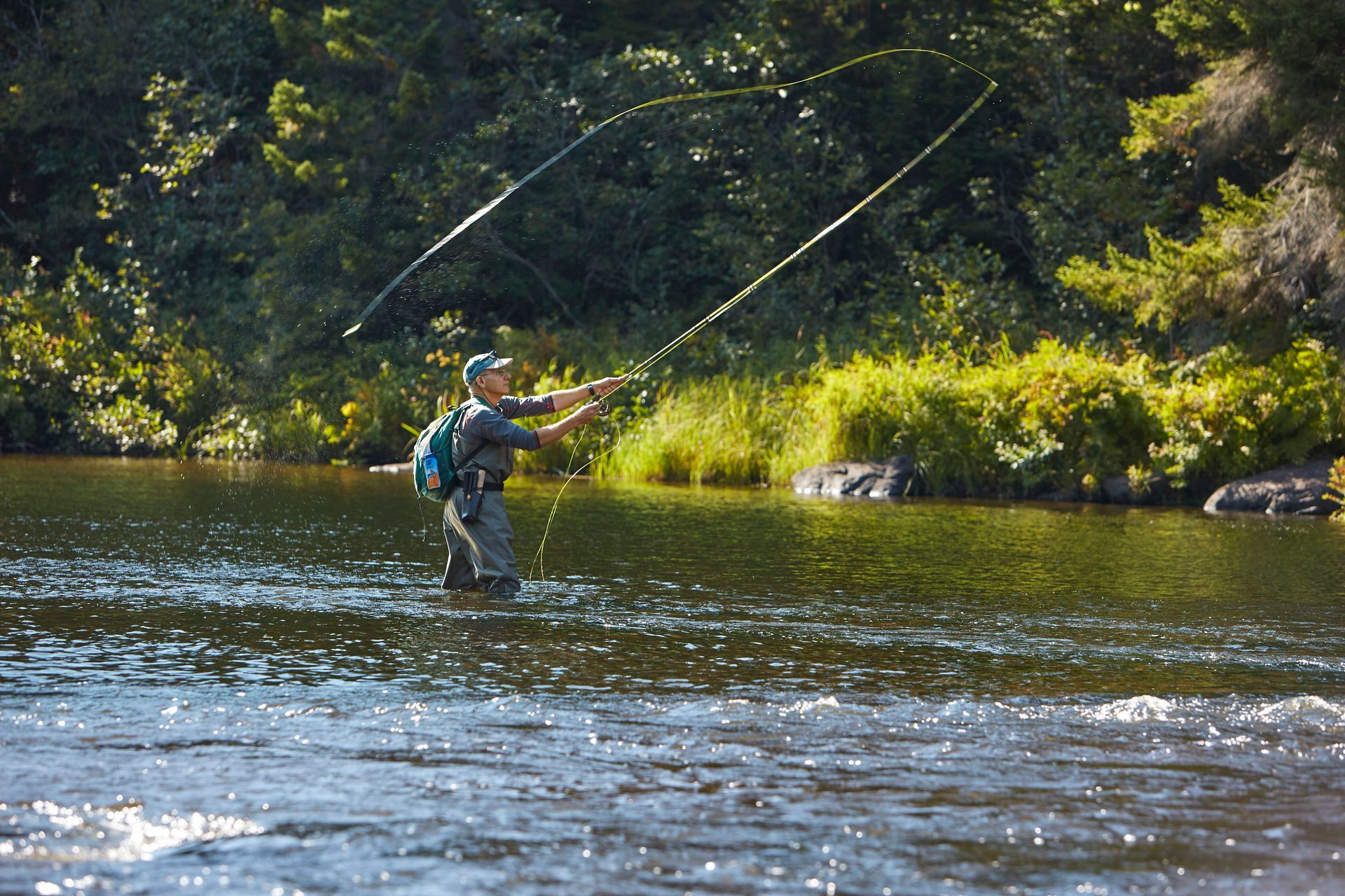 Person standing in a river, casting a fly fishing rod.