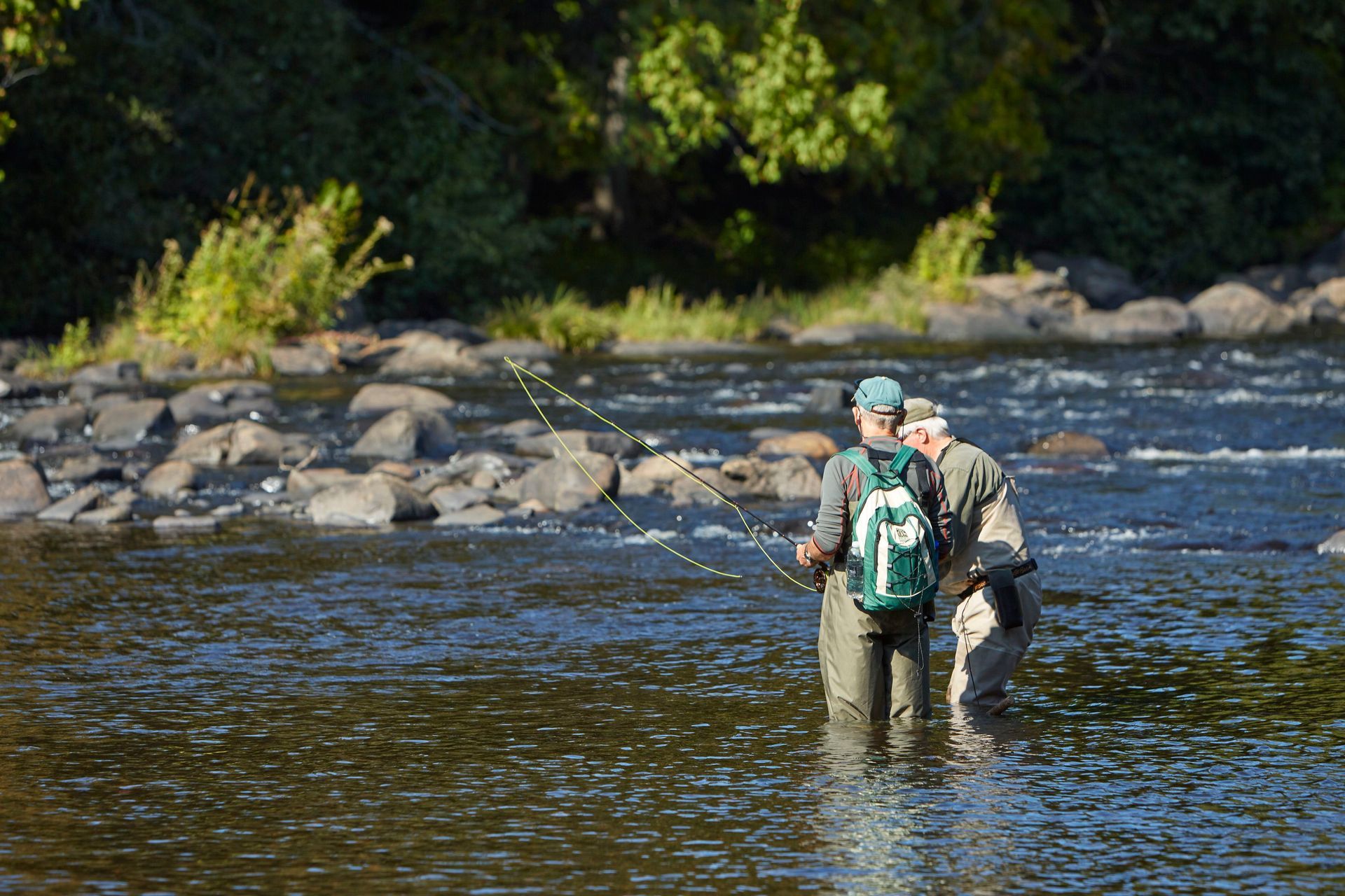 Two people standing in a river, fly-fishing.