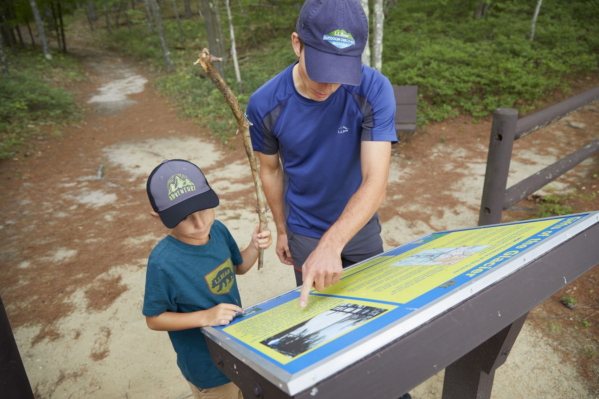 An instructor pointing to information on a kiosk, as a youth participant looks on.